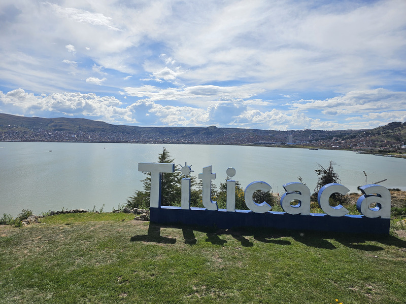 A sign saying 'Titicaca' overlooking a lake with the city of Puno behind