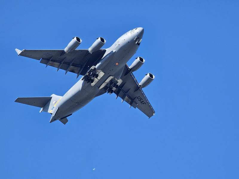 A C-17 flying overhead with gear extended